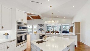 A modern kitchen with white cabinetry, a large island with a sink, stainless steel appliances, and a chandelier. - Spacious canal front home with private pool, dock & close to everything (Marco Island)
