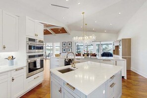 A modern kitchen with white cabinetry, a large island with a sink, stainless steel appliances, and a chandelier. - Spacious canal front home with private pool, dock & close to everything (Marco Island)