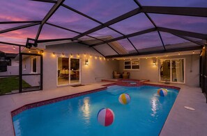 Ein Schwimmbad mit Glasumrandung, eine Terrassenfläche mit Sitzgelegenheiten und ein überdachter Bereich mit Lichterketten.