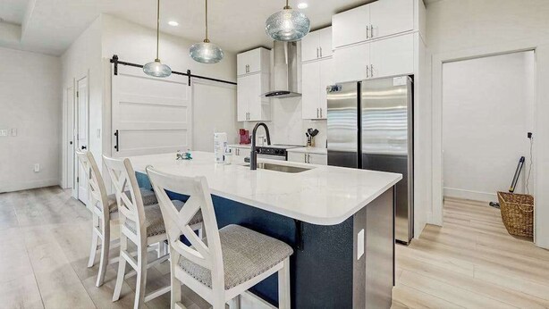 Una cocina moderna con una isla central, muebles blancos, electrodomésticos de acero inoxidable e iluminación colgante.