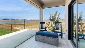 Un balcón con vista a la playa y al océano, muebles de mimbre y una puerta de cristal.