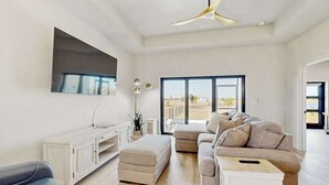 Una sala de estar moderna con sofá, reposapiés, televisor y ventilador de techo.