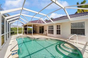 Ein Pool mit Glasveranda, eine überdachte Terrasse und ein Haus mit Ziegeldach.
