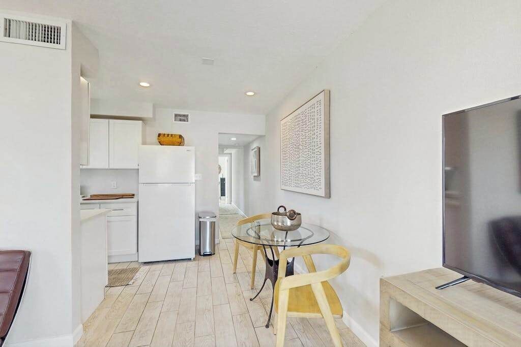 A modern kitchen with white cabinets, a dining table with chairs, a TV, and a framed artwork on the wall.