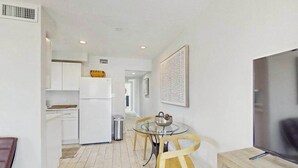 A modern kitchen with white cabinets, a dining table with chairs, a TV, and a framed artwork on the wall. - Cozy coastal duplex with full kitchen, close to beach & shopping (Naples)