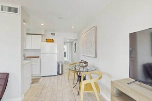 A modern kitchen with white cabinets, a dining table with chairs, a TV, and a framed artwork on the wall. - Cozy coastal duplex with full kitchen, close to beach & shopping (Naples)