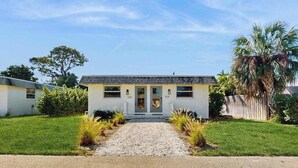 A single-story house with a front porch, a gravel driveway, and a well-maintained lawn. - Cozy coastal duplex with full kitchen, close to beach & shopping (Naples)