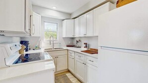 A kitchen with white cabinets, a stove, a sink, and a window. - Cozy coastal duplex with full kitchen, close to beach & shopping (Naples)