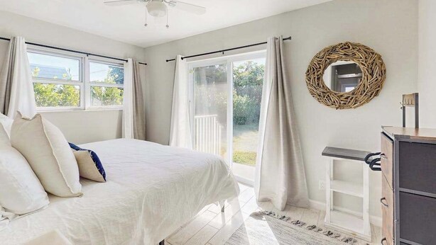 A bedroom with a bed, a ceiling fan, a dresser, and a view of the outdoors through a sliding door. - Cozy coastal duplex with full kitchen, close to beach & shopping (Naples)