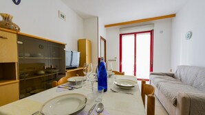 A dining area with a table set for four, a sofa, and a television in the background. - GuestHost - Alba Cozy Flat near the Sea W/Parking (Alba Adriatica)