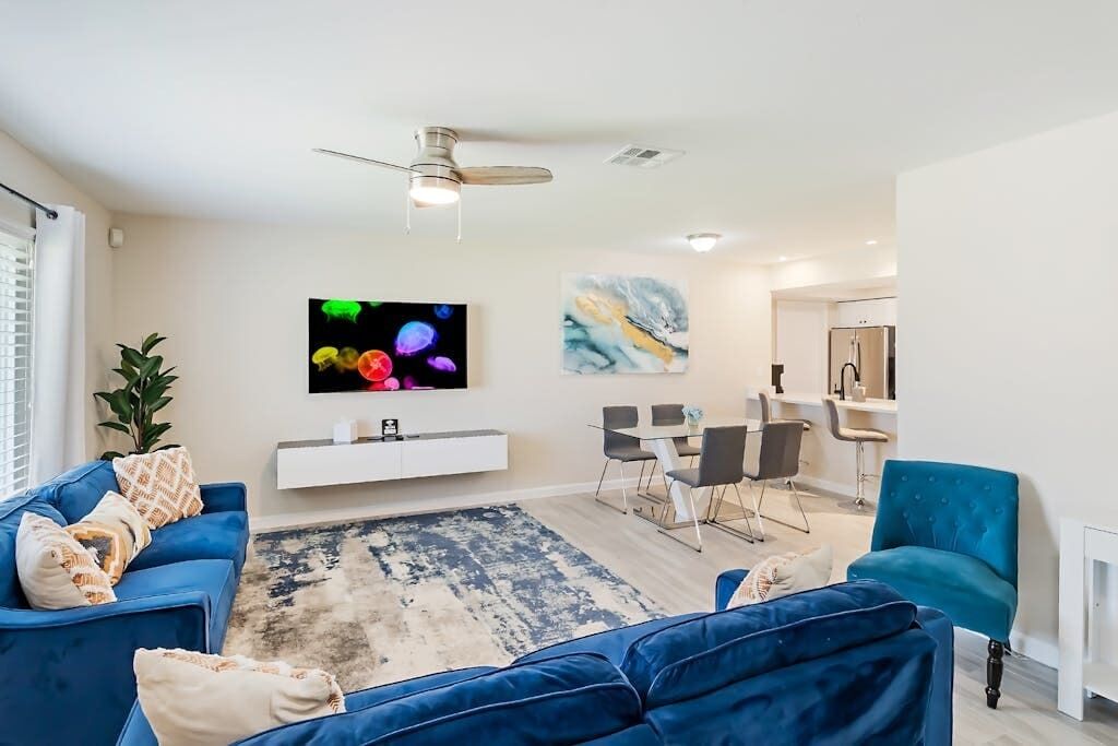 A modern living room with a blue sofa, a dining area with a white console table, and a ceiling fan.
