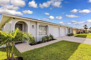 A row of single-story houses with a uniform architectural style, a well-maintained lawn, and a clear sky. - 6BR Cape Coral Duplex with Shared Pool & Dog-Friendly Yard (Cape Coral)