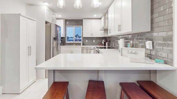 A modern kitchen with white cabinetry, a large island with stools, and pendant lighting. - Dog-friendly duplex with a patio, deck, washers, dryers, & central AC (Naples)