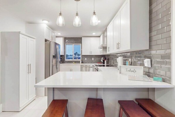 A modern kitchen with white cabinetry, a large island with stools, and pendant lighting. - Dog-friendly duplex with a patio, deck, washers, dryers, & central AC (Naples)