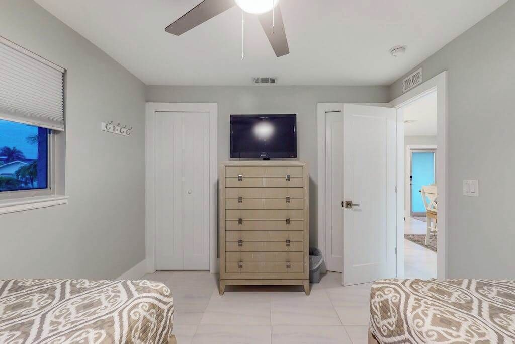 Quarto com cama, penteadeira, televisão e ventoinha no teto.