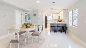 A modern kitchen with white cabinets, a central island with stools, and a dining area with a round table and chairs. - Dog-friendly duplex with a patio, deck, washers, dryers, & central AC (Naples)