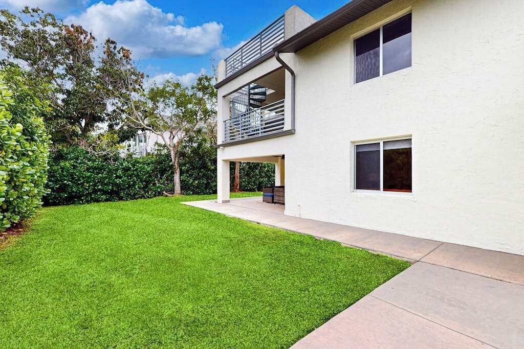 Une maison moderne à deux étages, dotée d’une pelouse bien entretenue, d’un balcon et d’un espace patio.