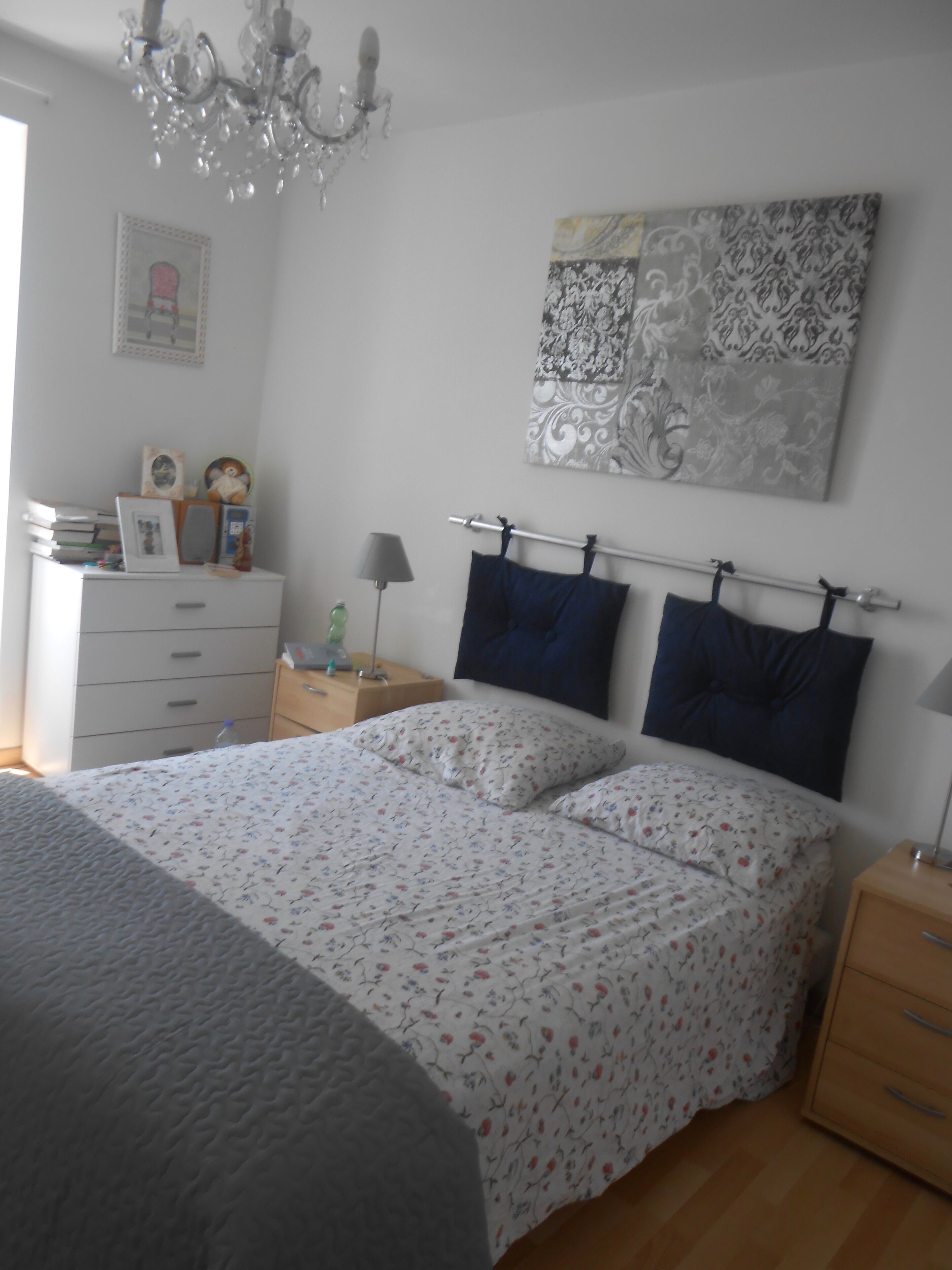 Une chambre à coucher comprenant un lit, des tables de chevet, une commode, un lustre, un tableau encadré et une décoration murale à motifs.
