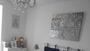 Ein Schlafzimmer mit einem Bett, Nachttischen, einer Kommode, einer Pendelleuchte, einem gerahmten Bild und einem Wandbehang mit Muster.