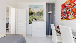 Ein modernes Hotelzimmer mit einem Bett, einem Schreibtisch mit Stuhl, einem Kleiderschrank, einem Poster an der Wand und einem farbenfrohen abstrakten Gemälde.