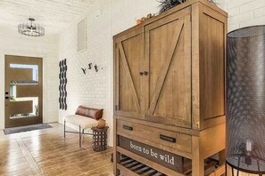 A wooden cabinet with the phrase 'born to be wild' on the front, a white brick wall, a leather bench, and a metal basket. - Dog friendly home with fire pit, enclosed yard, and washer and dryer (Cape Coral)