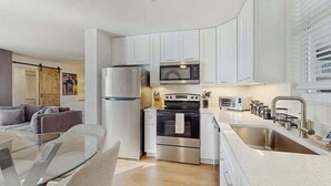 Una cocina moderna con armarios blancos, electrodomésticos de acero inoxidable, una mesa de comedor de vidrio y vistas al área de estar.