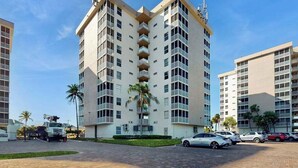 Un hotel de varios pisos con balcones, estacionamiento y palmeras.