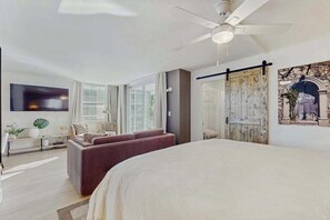 A modern hotel room with a large bed, a seating area with a sofa and chairs, a ceiling fan, and a large window. - Gorgeous condo with modern upgrades, Gulfviews & shared pool (Bonita Springs)