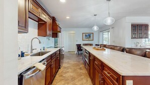 A modern kitchen with wooden cabinets, a large island, and a dishwasher. - Snowbird Retreat – Canal Home w/Pool, Game Room & Pet Friendly (Punta Gorda)