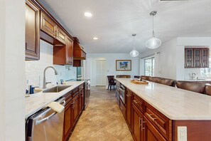 A modern kitchen with wooden cabinets, a large island, and a dishwasher. - Snowbird Retreat – Canal Home w/Pool, Game Room & Pet Friendly (Punta Gorda)