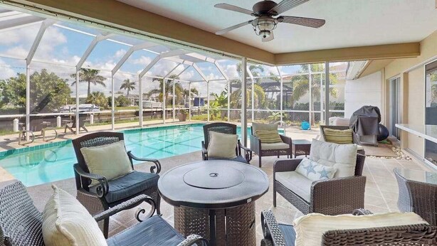A covered outdoor area with a pool, wicker furniture, and a ceiling fan. - Snowbird Retreat – Canal Home w/Pool, Game Room & Pet Friendly (Punta Gorda)