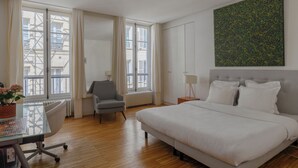 A hotel room with a bed, a desk, a chair, a radiator, and a window with curtains. - Paris Opera Prestige residence (Paris)