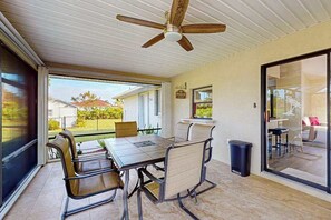 Ein offener Wohnbereich mit Esstisch, Stühlen, Deckenventilator und einer Glastür, die auf eine Terrasse führt.