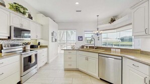 Una cocina moderna con armarios blancos, electrodomésticos de acero inoxidable y un amplio ventanal con vistas al exterior.