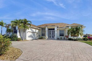 A two-story house with a tiled roof, a front entrance with a glass door, and a paved driveway. - Serene and elegant with heated pool, water views, family and dog friendly, W/D (Port Charlotte)