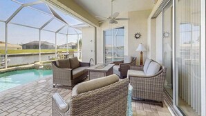 Un patio techado con mobiliario de mimbre, un ventilador de techo y vistas a una piscina.