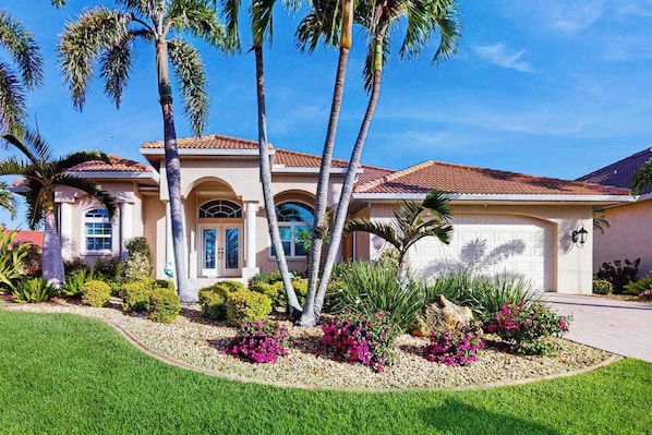 A residential house with a garage, palm trees, and a well-maintained garden.