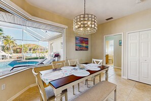 A dining area with a view of a swimming pool, a chandelier, and a painting on the wall.