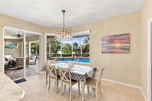 Zona pranzo con vista piscina, ventilatore a soffitto e un quadro appeso al muro.