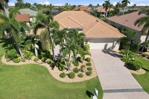 A residential property with a tiled roof, a driveway, and a landscaped garden with palm trees and shrubs.