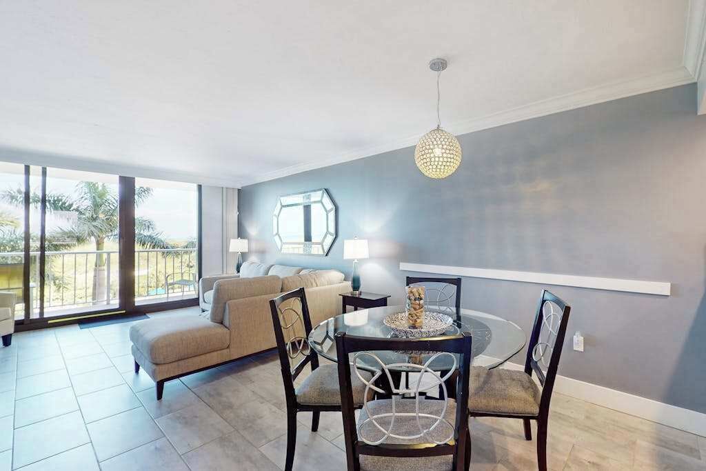 A modern living room with a dining table, chairs, a sofa, and a large window with a view.