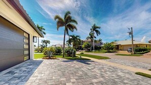 A residential driveway with a paved walkway, palm trees, and houses in the background. - Dazzling coastal home with private pool & spa, lanai, AC, W/D, WiFi (Marco Island)