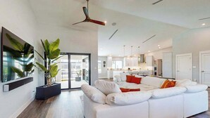 A modern living room with a white sofa, a ceiling fan, and a large plant. - Dazzling coastal home with private pool & spa, lanai, AC, W/D, WiFi (Marco Island)