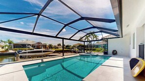 A swimming pool with a covered area, a lounge chair, and a view of surrounding houses. - Dazzling coastal home with private pool & spa, lanai, AC, W/D, WiFi (Marco Island)