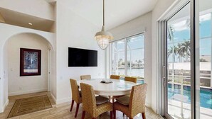 Un coin repas avec une table ronde, des chaises en osier, un téléviseur à écran plat et une vue sur une piscine.