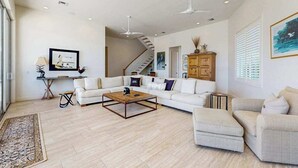 Un salon spacieux avec un grand canapé blanc, une table basse et un escalier menant à un autre niveau.