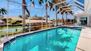 Une piscine entourée de parois en verre, agrémentée de palmiers et offrant une vue sur d’autres bâtiments.
