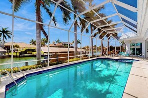 A swimming pool with a glass enclosure, palm trees, and a view of other buildings. - Dog-friendly waterfront getaway with lanai, private pool, & pool spa (Marco Island)