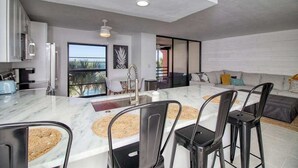 A modern kitchen with a marble island, black bar stools, and a view of the outdoors. - Amazing oceanfront condo with pool, hot tub, tennis, & stunning balcony views (Marco Island)
