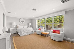 Une chambre spacieuse avec une grande fenêtre, un lit, deux tables de chevet, une chaise et une petite table.